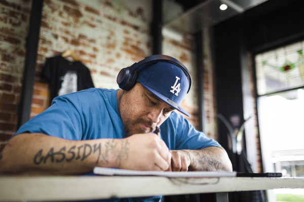 Man sitting at table with headphones on, writing in notebook