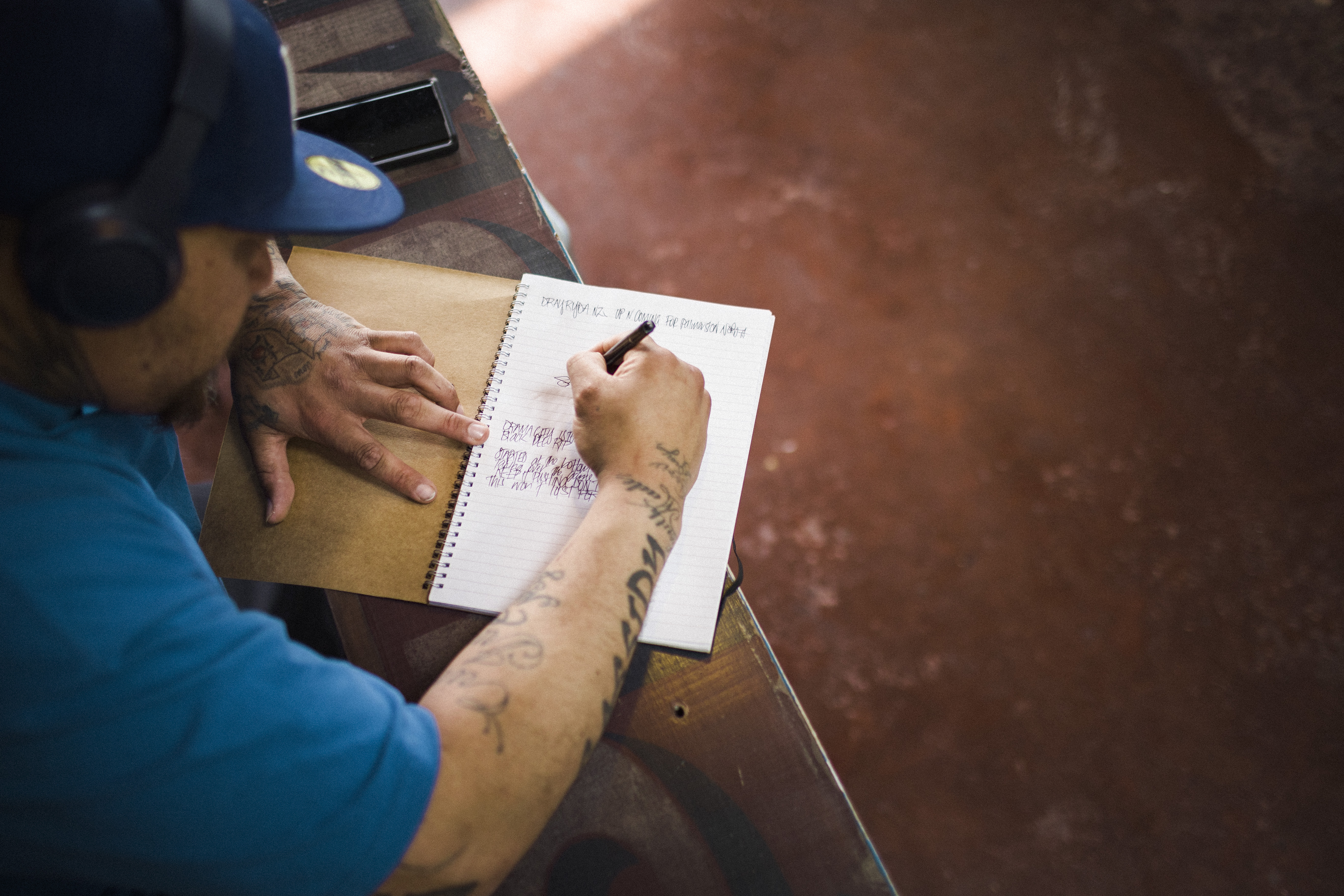 Man wearing headphones sitting at a table writing in notebook