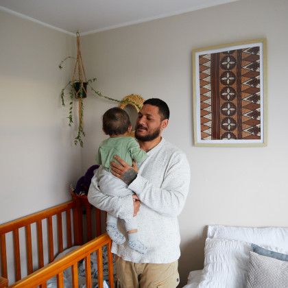Man holding a baby, smiling, with a cot in the background.