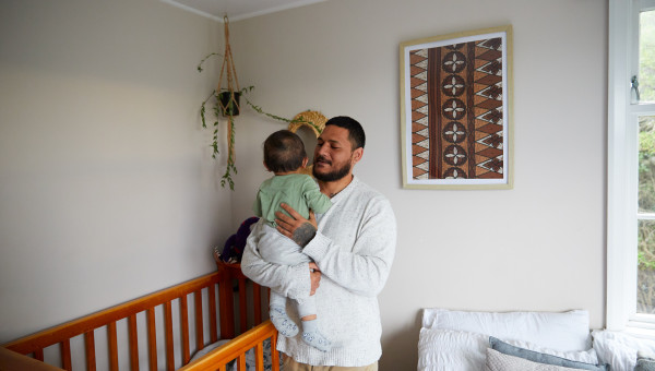 Man holding a baby, smiling, with a cot in the background.
